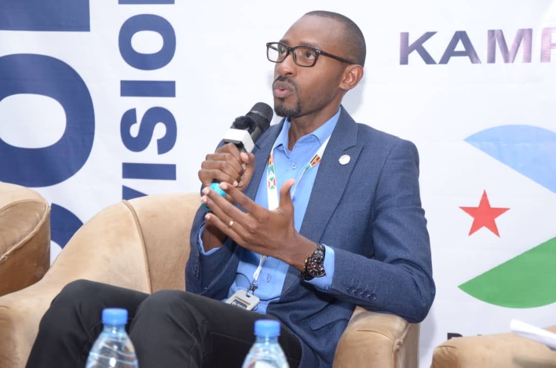 Back of a man at a concert. Hes wearing a beanie hat and a baggy denim jacket with studs. Photo with a purple hue
